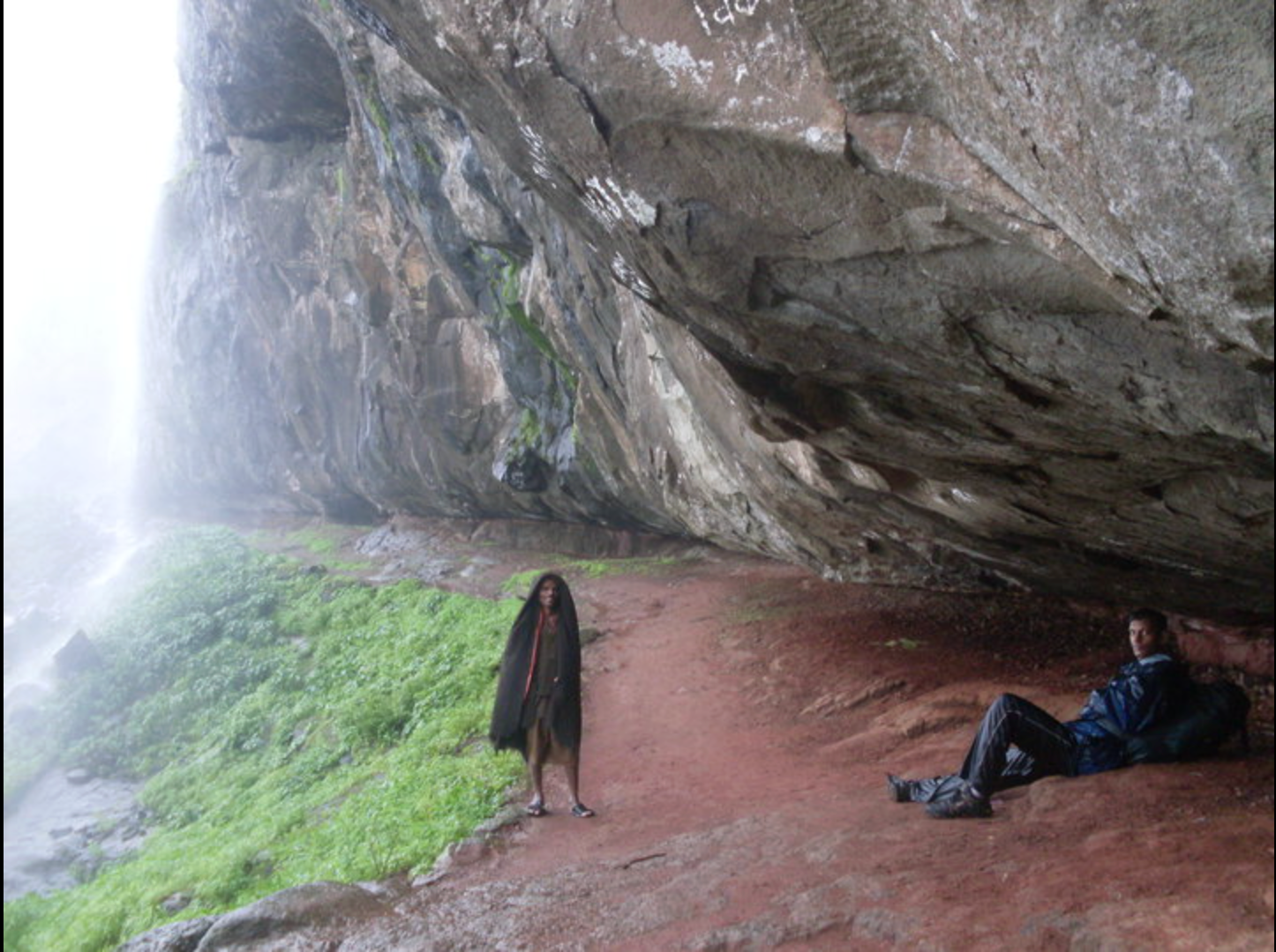 Two trekkers at the base of the dramatic cliff face on the descent from Harishchandragad to Pachnai
