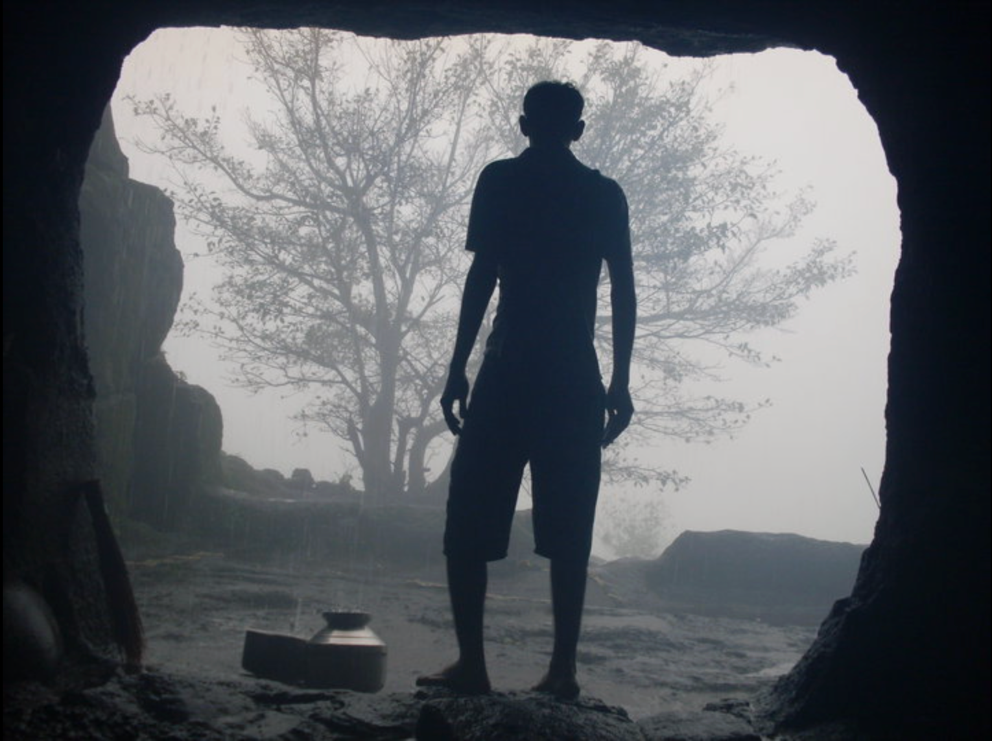 Silhouette of a trekker standing inside the cave at Harishchandragad with a wall of monsoon fog outside